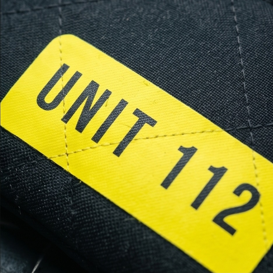 Detailaufnahme: UNIT 112 Patch auf gestepptem dunkelblauem Feuerwehrstoff aus Einsatzkleidung. Echte Handarbeit: Gelber UNIT 112 Aufnäher auf recyceltem Feuerwehrstoff als Geschenkidee.