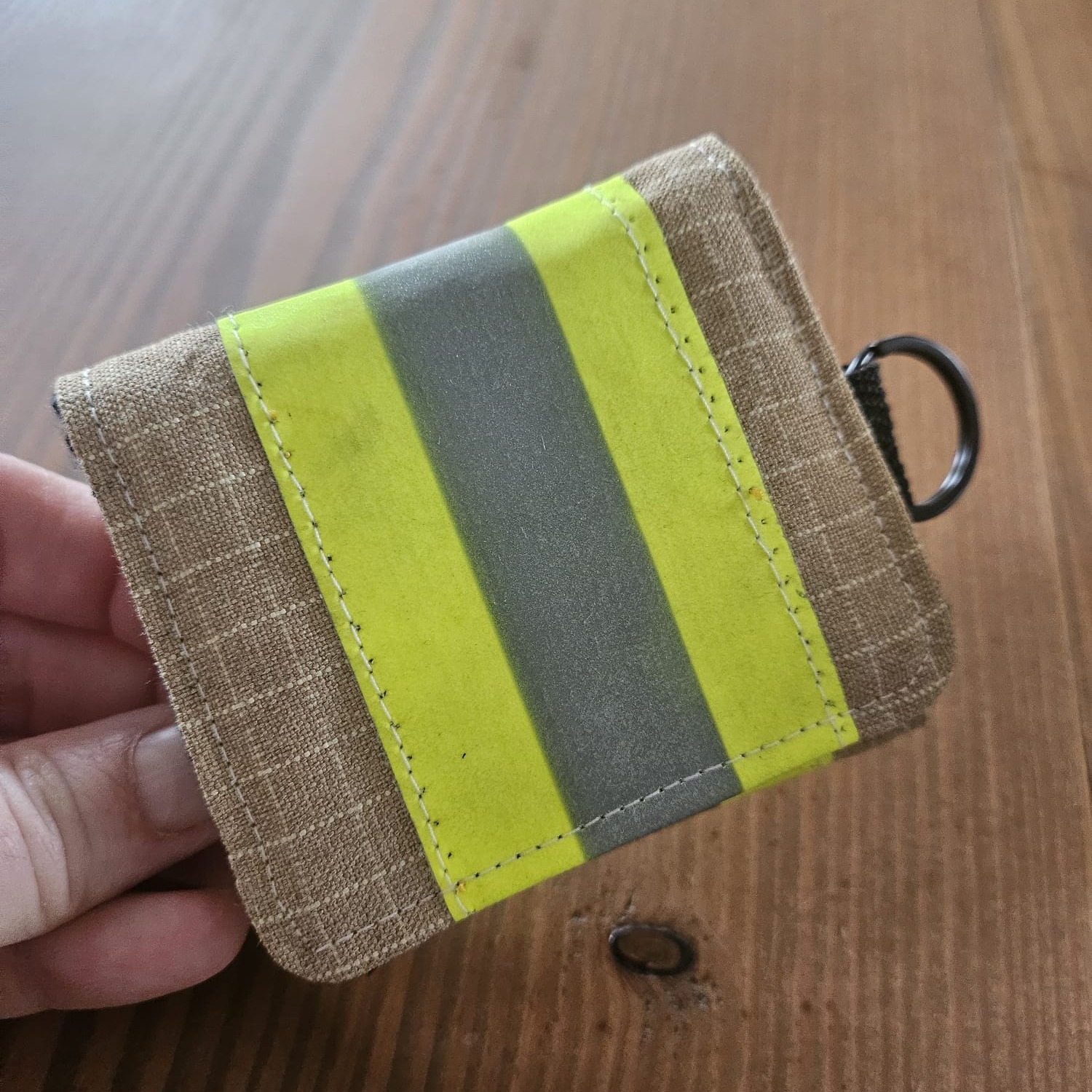Quadratisches 8x8 cm Notfall-Täschchen aus sandfarbenem Feuerwehrstoff mit gelb-silbernem Reflexstreifen.