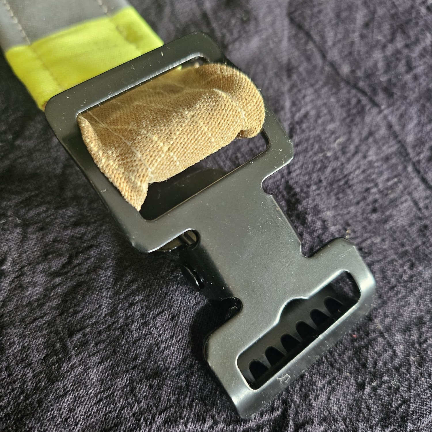Detailansicht einer schwarzen Metallschnalle auf beigem Feuerwehr-Einsatzstoff mit robuster Naht und Teilen eines orangefarbenen Reflektors.
