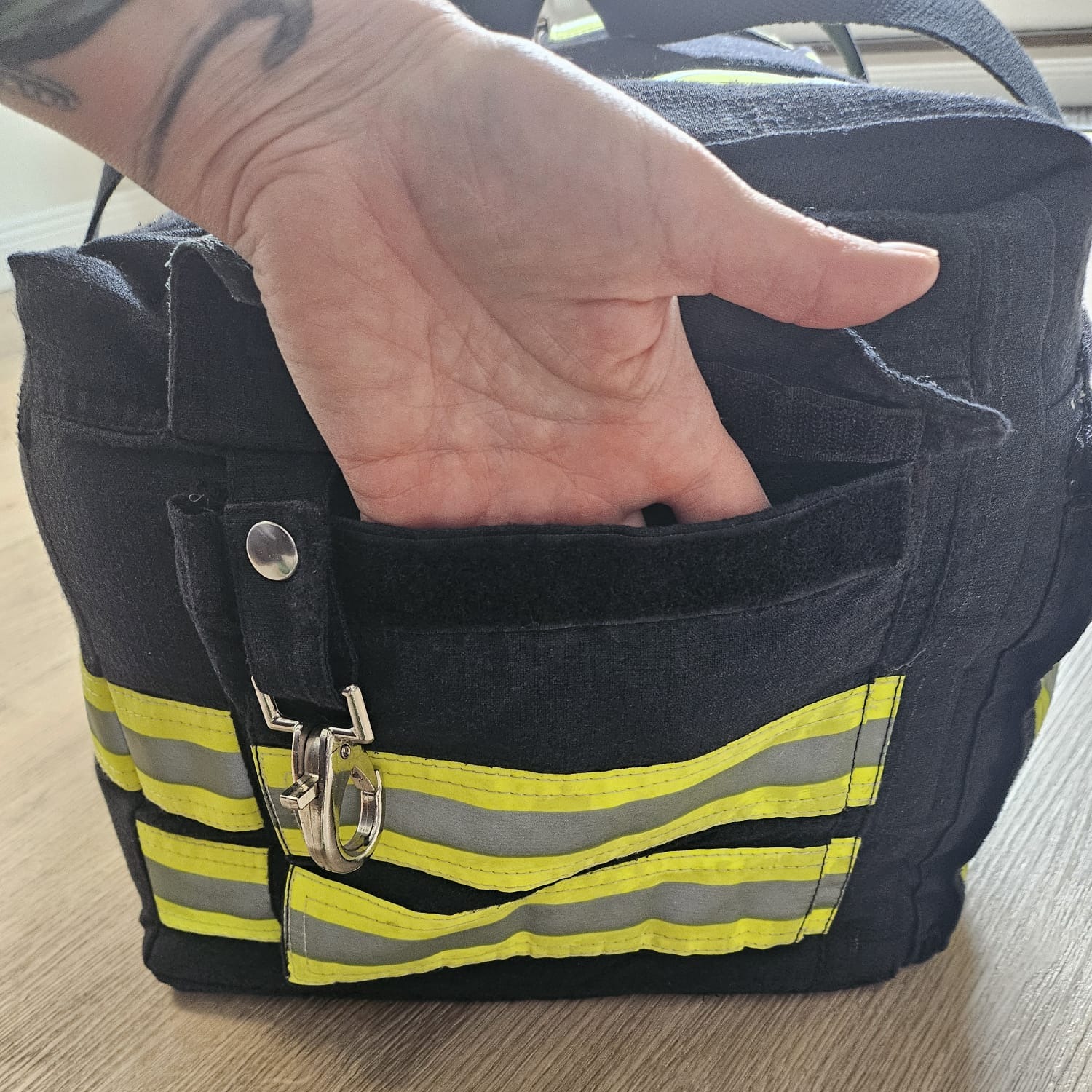 Eine Hand greift in das geöffnete Seitenfach einer dunkelblauen Feuerwehr-Tasche mit Klettverschluss und Karabiner