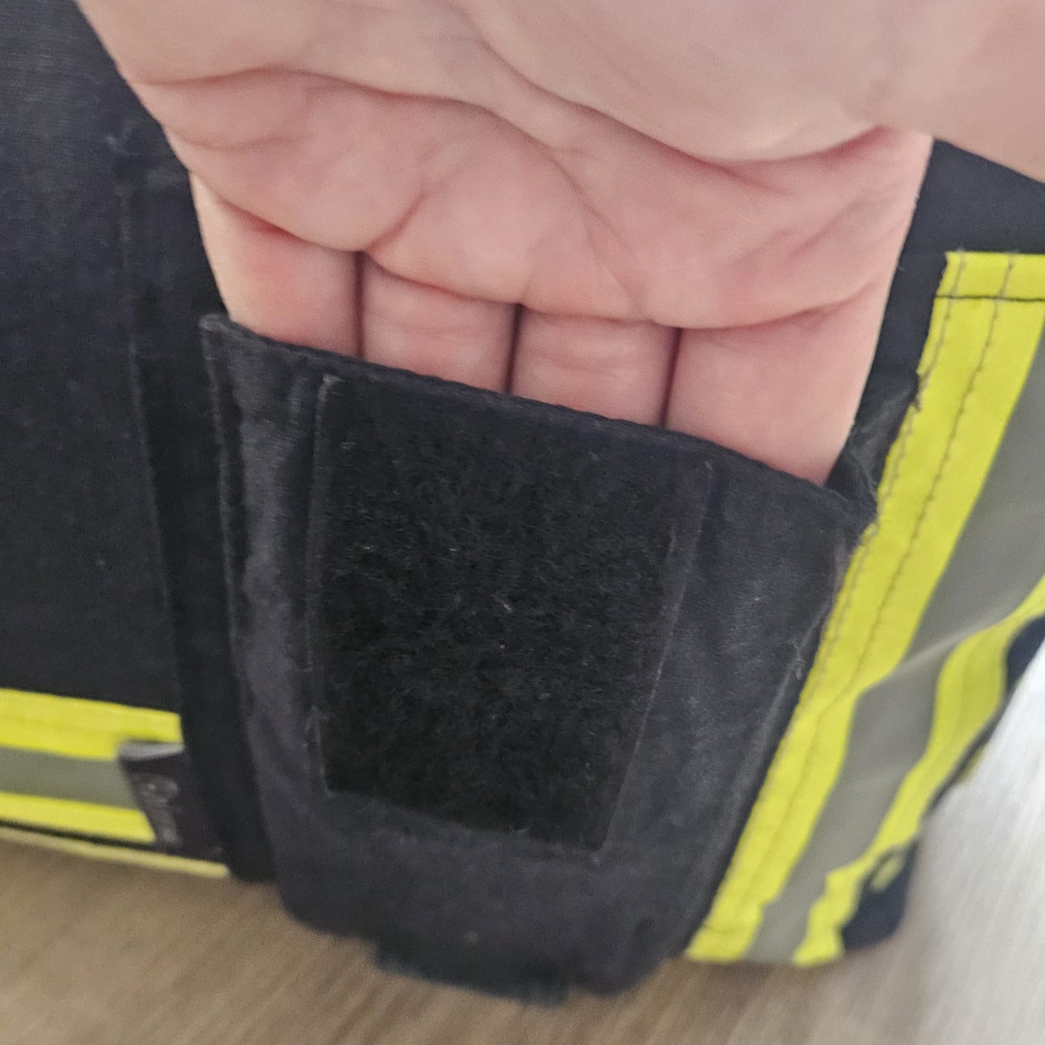 Eine Hand greift in ein kleines Außenfach mit Klettverschluss an einer dunkelblauen Feuerwehr-Tasche