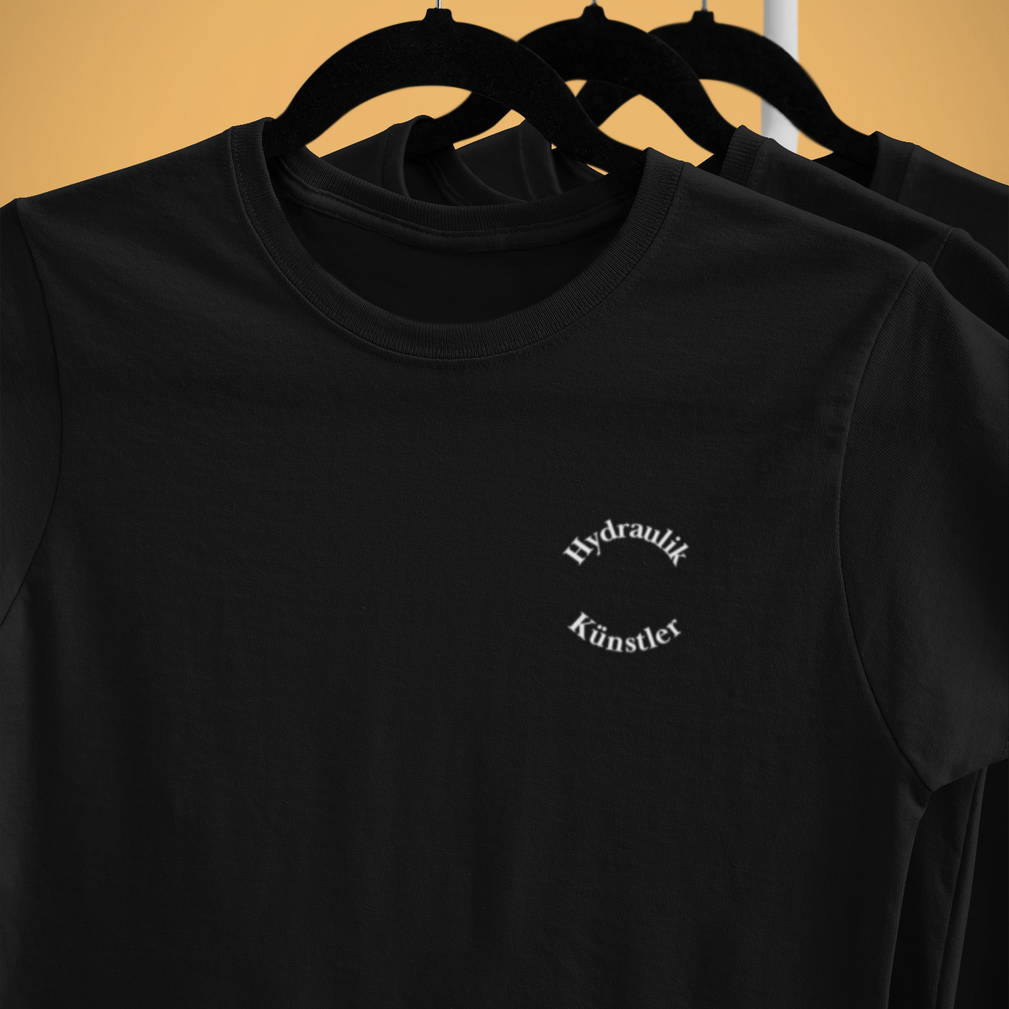 Detailansicht des runden weißen Brustdrucks Hydraulik Künstler auf einem schwarzen Feuerwehr T-Shirt. Hochwertige Veredelung von AWesome.