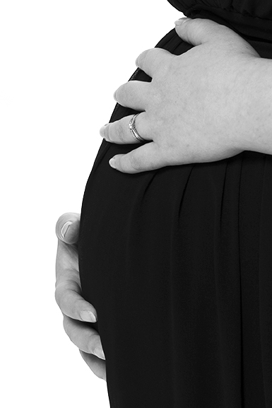 Photographie noir et blanc, studio gros plan de deux mains sur un ventre rond de profil. Robe noire et fond blanc