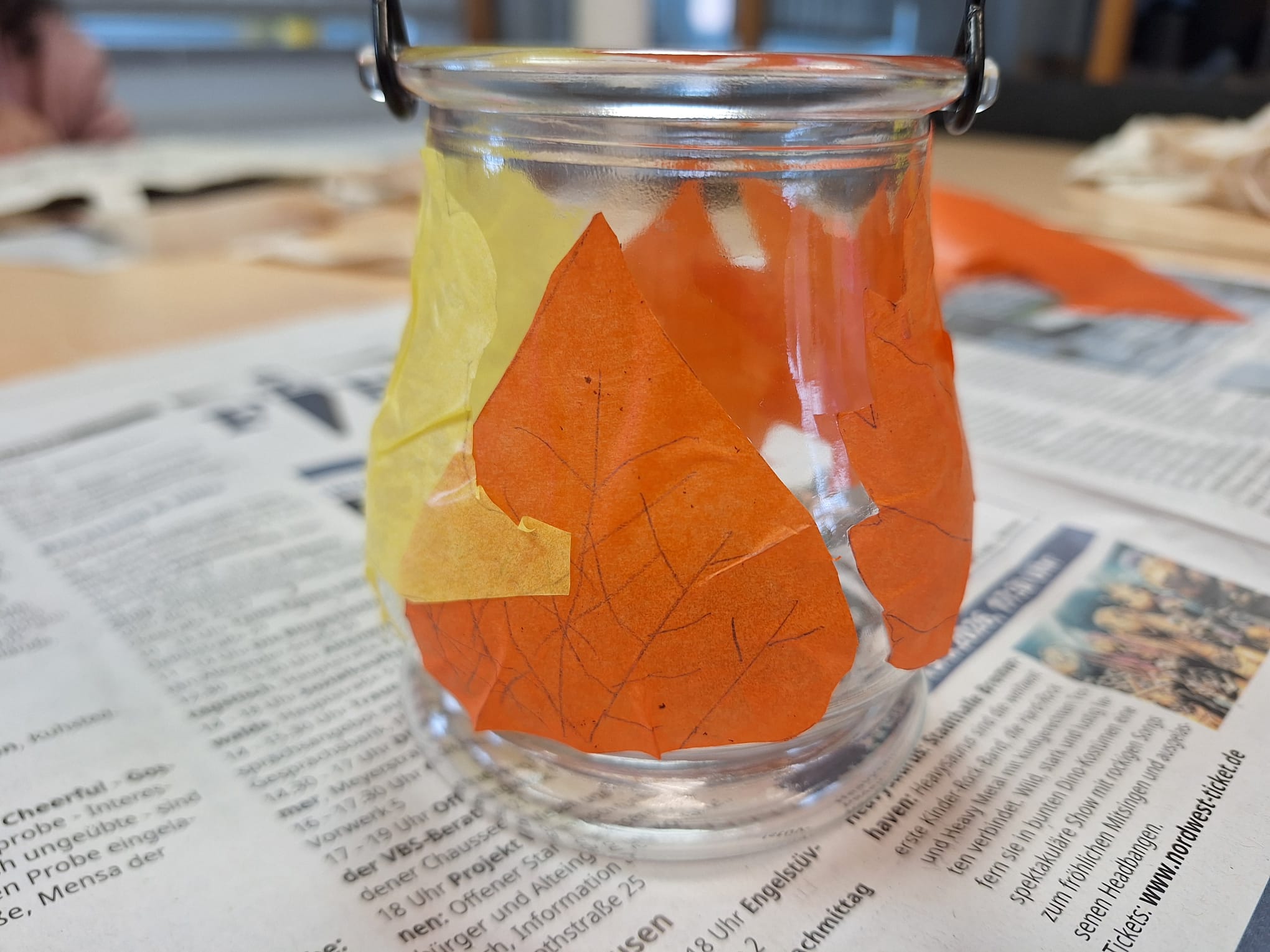 Ein Windlicht wurde mit Laub aus buntem Transparentpapier beklebt.