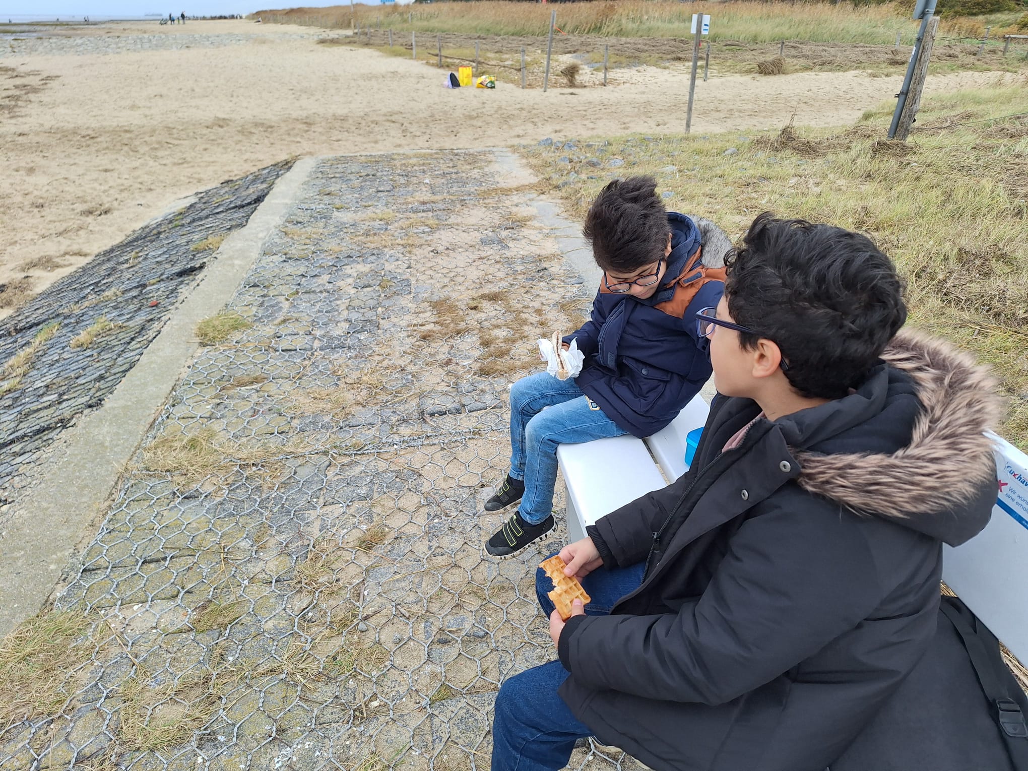 Zwei Jungs sitzen auf einer Bank am Strand und essen.