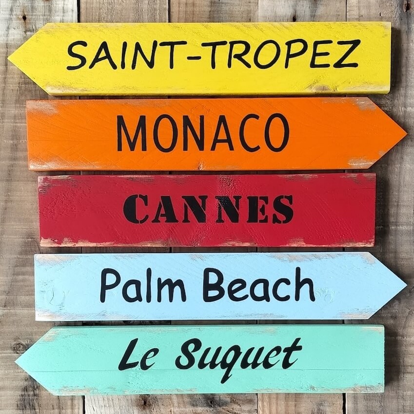 Panneaux directionnels en bois multicolores, écritures différentes peintes en noir indiquant des villes du sud de la France
