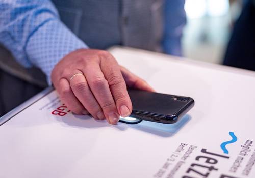 Eine Hand hält ein Smartphone mit dem Display nach unten über einen Scanner, der in einem SelfPrint-Kiosk verbaut ist.