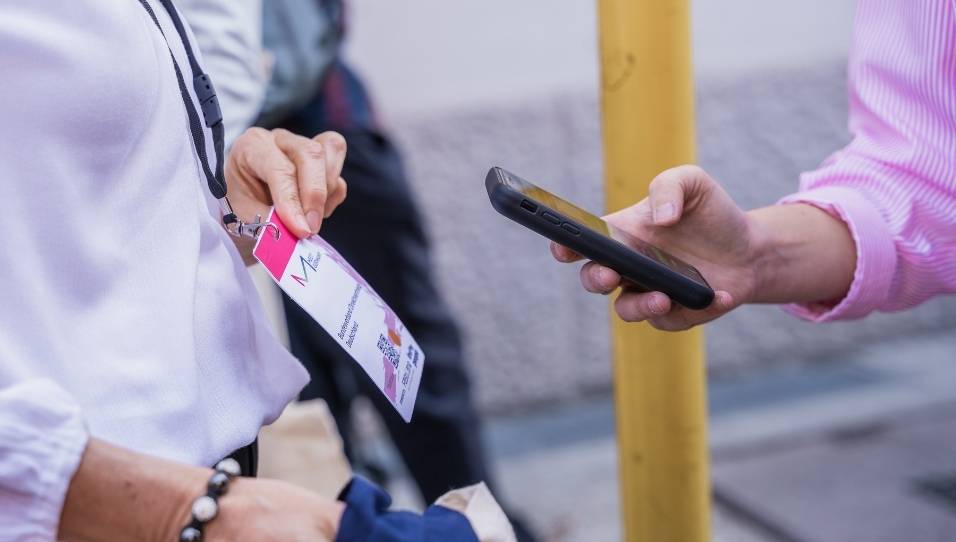 Eine Hand hält ein Smartphone. Auf dem Smartphone ist die FastEntry-App geöffnet. Das Smartphone scannt einen QR-Code auf dem Namensschild.