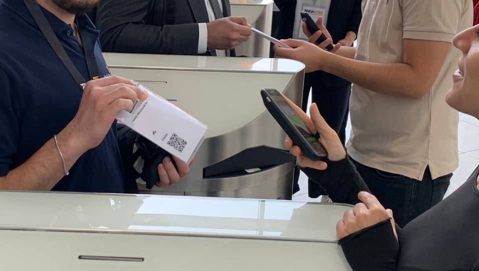 Eine Hand hält ein Smartphone. Auf dem Smartphone ist die FastEntry-App geöffnet. Das Smartphone scannt einen QR-Code auf dem Namensschild.