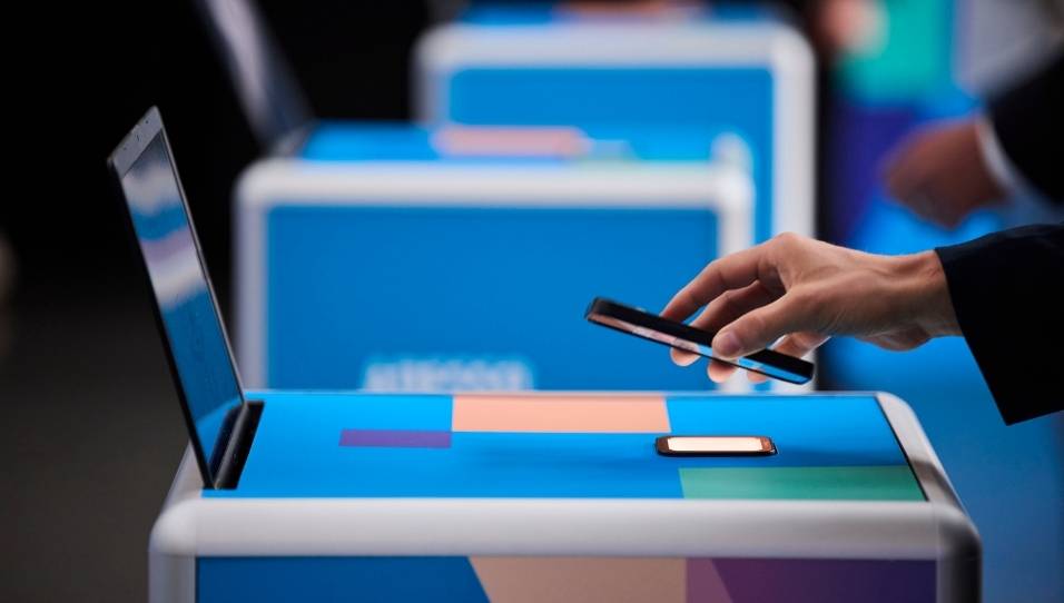 Nahaufnahme von einem SelfPrint Kiosk. Eine Hand hält ein Smartphone über den Scanner des Kiosks und scannt einen QR-Code ein.