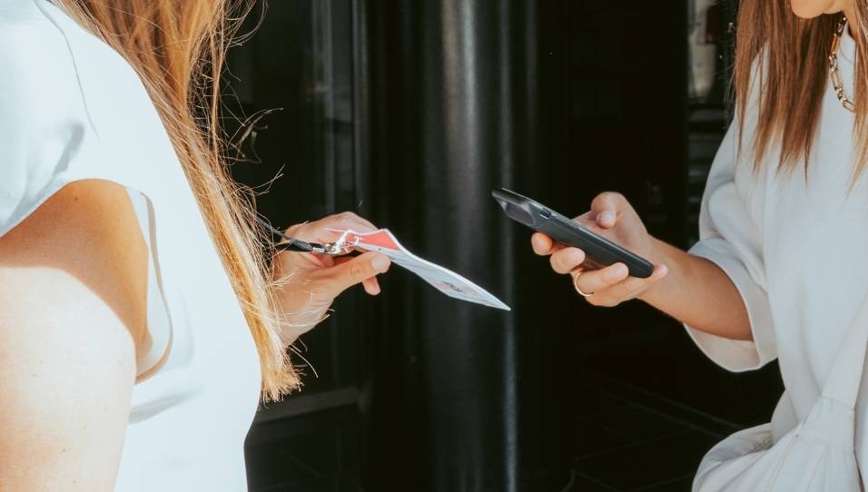 Eine Hand hält ein Smartphone. Auf dem Smartphone ist die FastEntry-App geöffnet. Das Smartphone scannt einen QR-Code auf dem Namensschild.