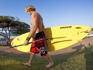 Robby Naish trägt sein SUP Board an den Strand