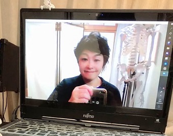 ノートノートパソコンの画面の中でボイストレーナーの荒井みな子がほほえんでいる,オンラインレッスンをしている