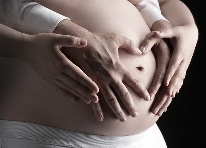 Die schwangere Frau und ihr Partner bilden ein Herz mit ihren Händen auf dem Babybauch