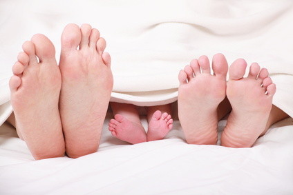 Die Füße von Mutter, Vater und Kind liegen unter der Bettdecke