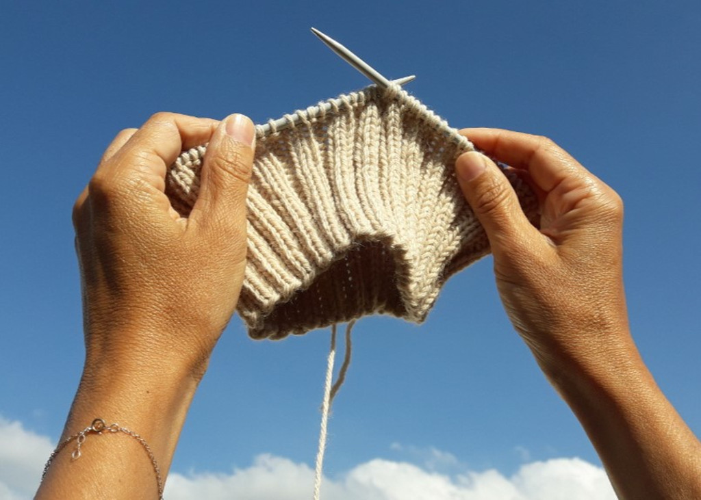 Hands show part of the knitting process of a handmade wool hat.