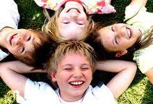 Vier Kinder liegen auf dem Boden und lachen in die Kamera.