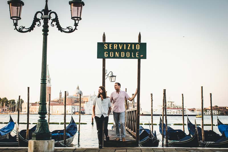 Venice engagement photo of an LGBTQ+ couple exchanging affectionate looks in St. Mark's Square.