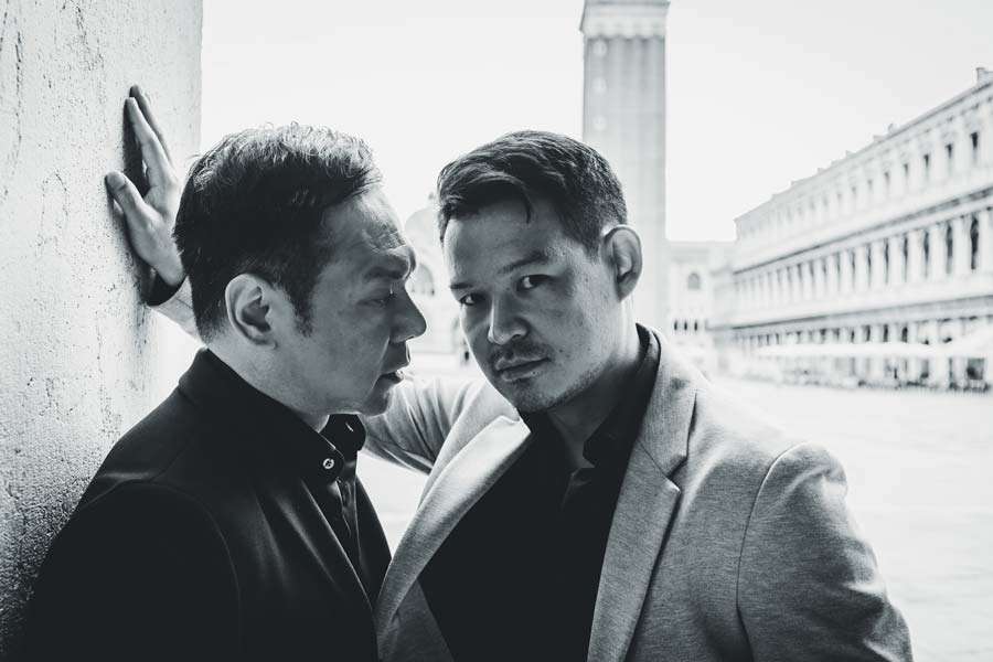 Gay couple holding hands in front of Basilica di San Marco during golden hour