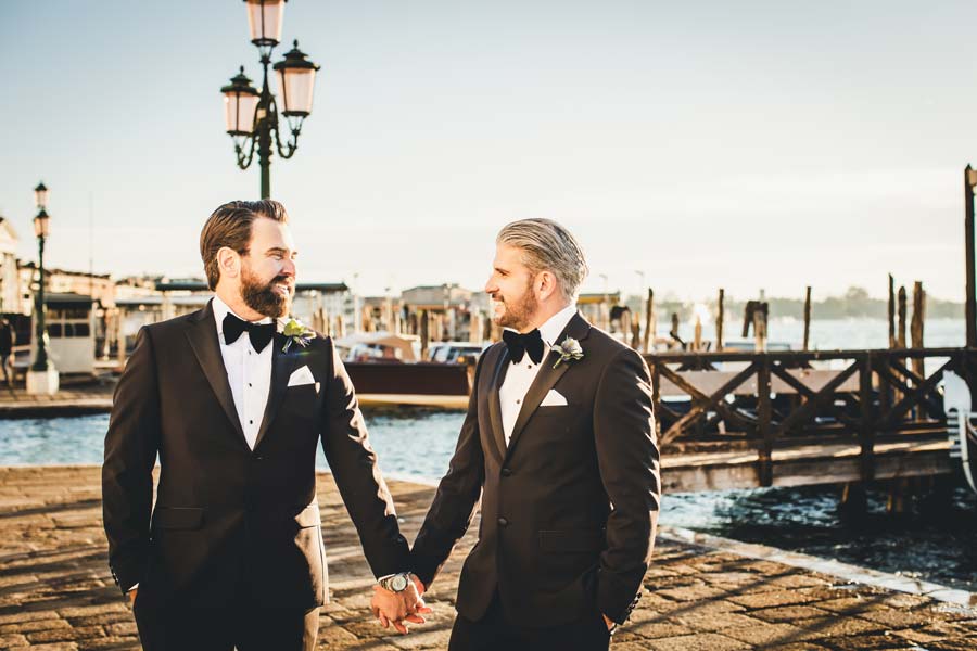 Romantic gay couple eloping in Venice, holding hands near a canal.