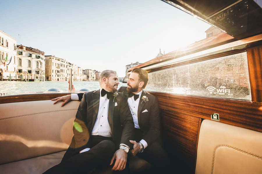 LGBTQ+ couple sharing a kiss on a private water taxi in Venice.