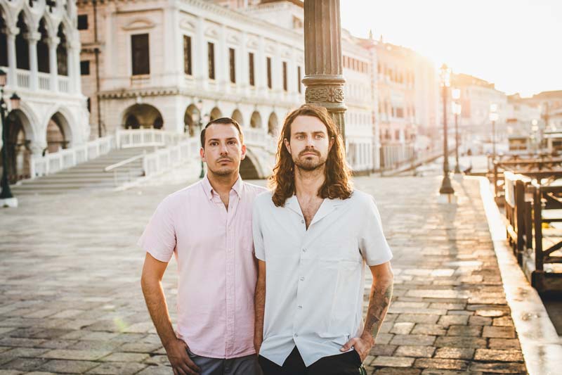 Engaged LGBTQ+ couple poses for a portrait in a picturesque, uncrowded alley in Venice.