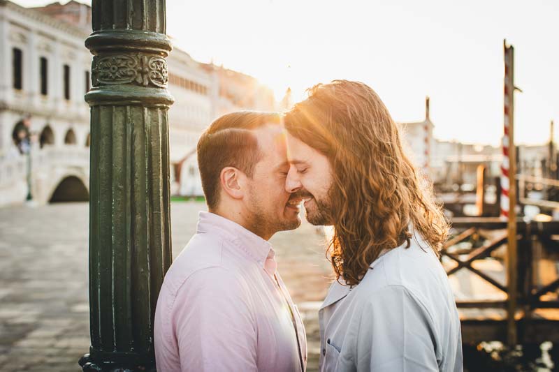 LGBTQ+ couple in Venice passionately kissing on a bridge during an engagement photoshoot.