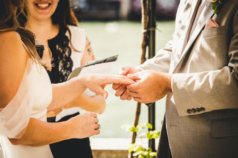 A close-up of the couple's hands holding their wedding rings, with the detailed patterns of the hotel's wallpaper.