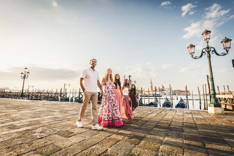 Three sisters running across a small Venetian bridge in morning light
