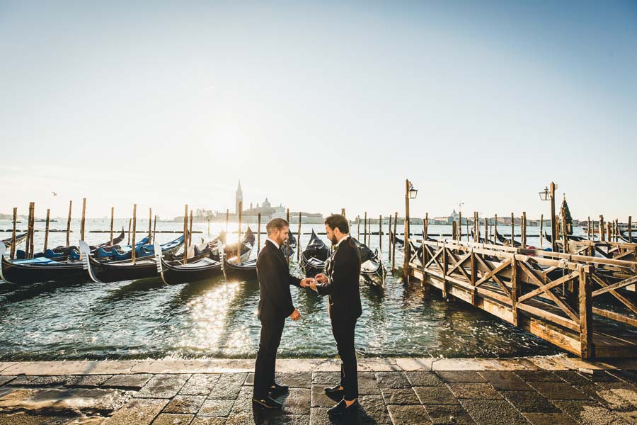 Gay couple exchanging wedding vows with gondolas in the background.