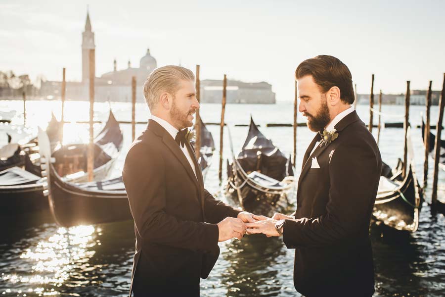 Gay couple exchanging vows on Riva degli Schiavoni with the lagoon in the background.