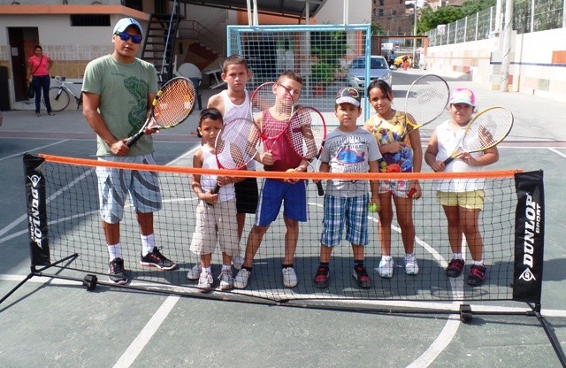 Un grupo de niños que aprenden a jugar tenis en las canchas del Patronato municipal, posando con su entrenador. Manta, Ecuador.