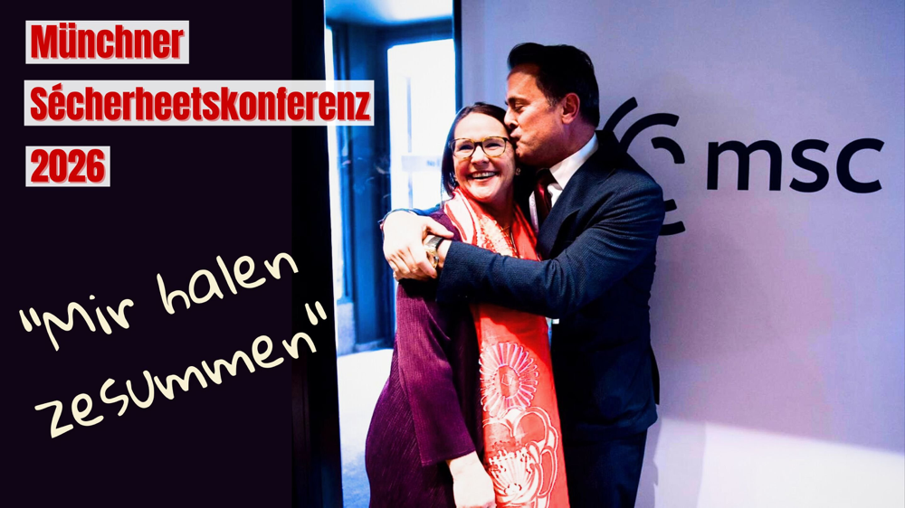 D’Verdeedegungsministesch Yuriko Backes an den Ausseminister Xavier Bettel ëmarmen sech virum Logo vun der Münchner Sécherheetskonferenz. D’Szen weist Zesummenhalt am diplomatesche Kontext.