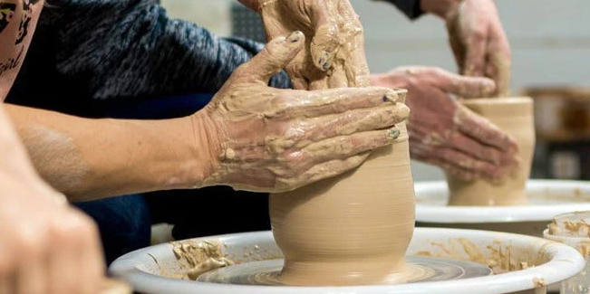 Messy hands working with clay on the pottery wheel
