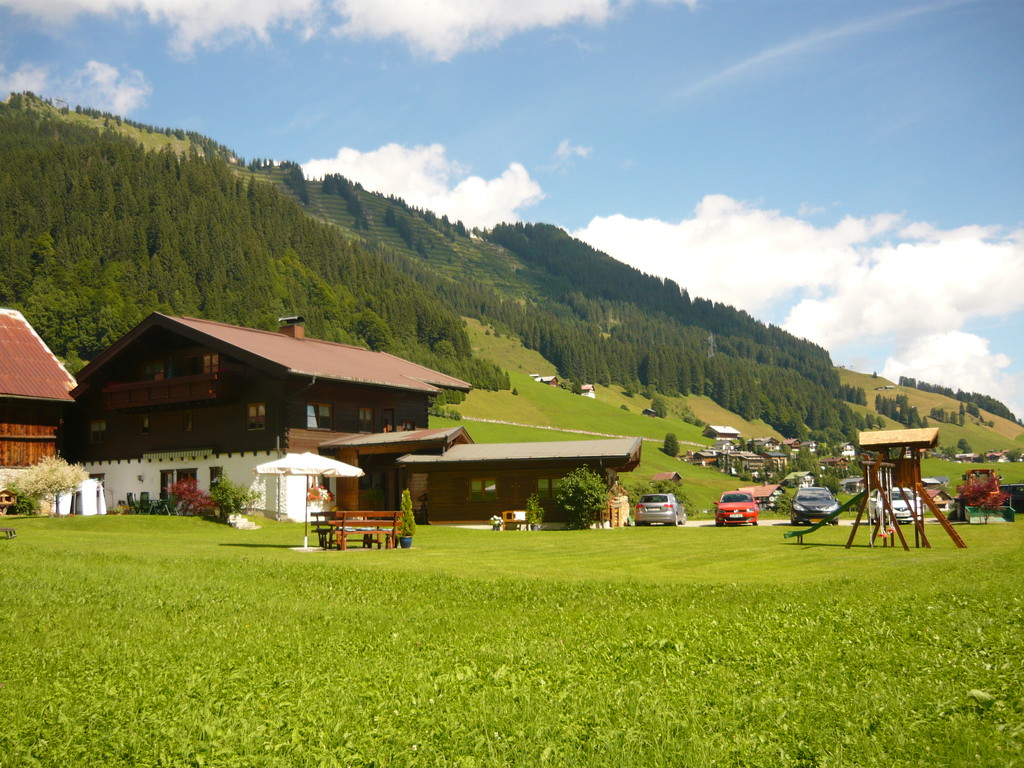 Haus Rückansicht im Sommer mit Spielplatz, Sitzmöglichkeiten und großer Liegewiese