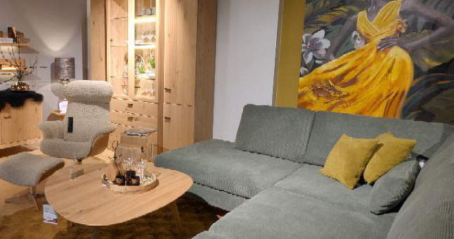 Grünes Cord-Sofa und beiger Sessel in modernem Wohnzimmer mit Holzschrank und Kunst.
