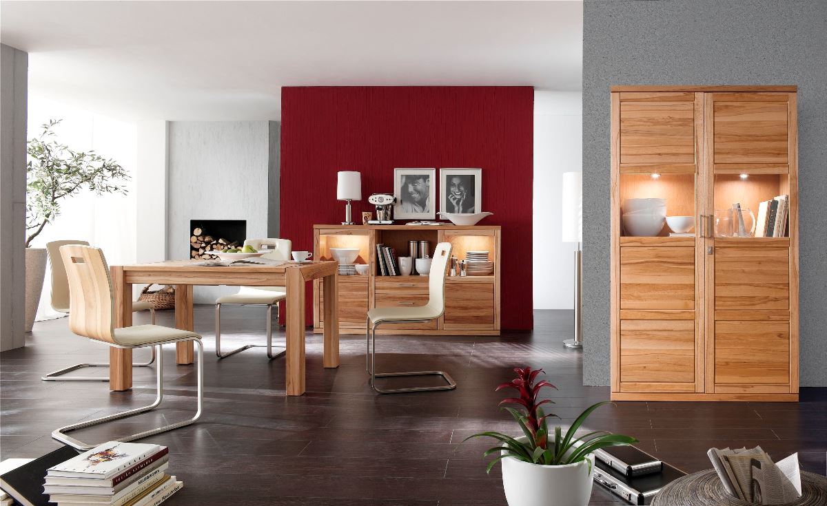 Esszimmer mit Holztisch und Stühlen, Kommode vor roter Wand und beleuchtetem Schrank.