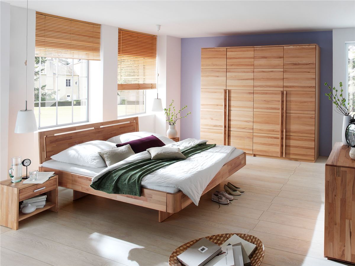 Helles Schlafzimmer mit niedrigem Holzbett, großem Holzschrank, hellen Böden und Jalousien.