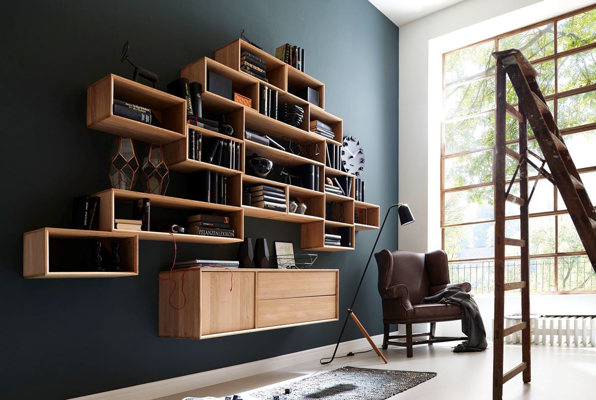 Modernes, gestaffeltes Hängeregal aus hellem Holz, Sideboard, Ledersessel und Fenster.