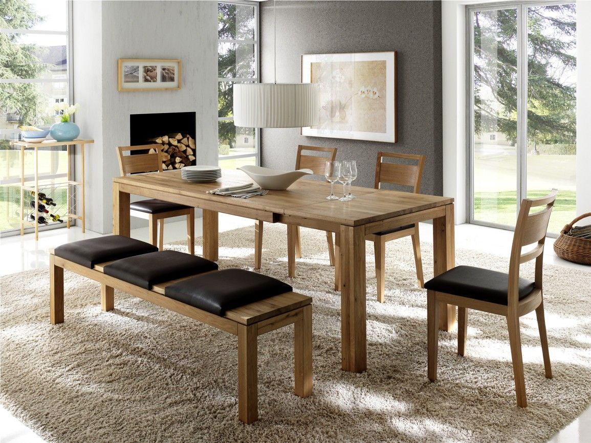 Esszimmer mit Holztisch, Holzbank und Stühlen mit dunklem Lederpolster auf beigefarbenem Teppich.