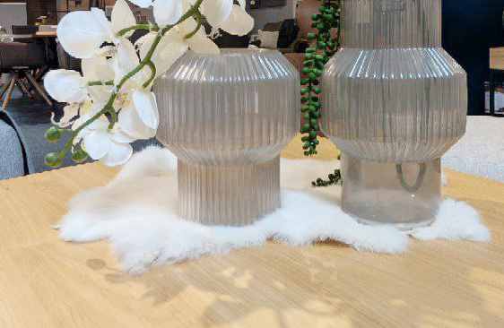 Gerippte Glasvasen auf einem Holztisch, dekoriert mit einer weißen Kunstfellunterlage und Orchideen.