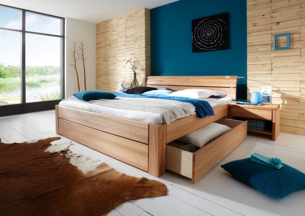 Holzbett mit Stauraumschubladen in modernem Schlafzimmer mit blauer Akzentwand und Fellteppich.