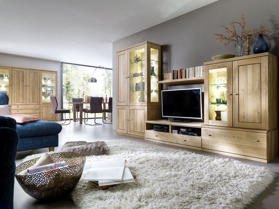 Wohnzimmer mit Esstisch im Hintergrund, einer Regalwand aus Holz und einem flauschigen Teppich.