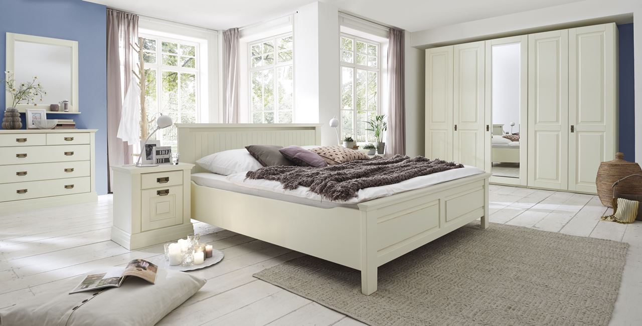 Helles, cremefarbenes Schlafzimmer im Landhausstil mit Bett, Kommode und großem Schrank.