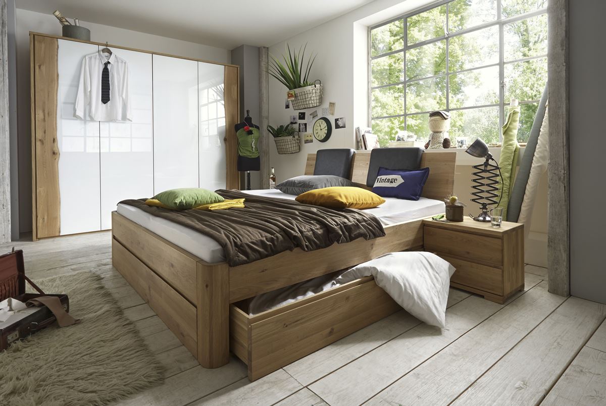 Holzbett mit Stauraumschublade, weißem Kleiderschrank und hellem, großem Fenster im Raum.