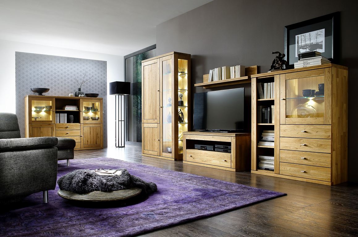 Wohnzimmer mit Massivholzmöbeln, lilafarbenem Teppich und einem grauen Sofa.