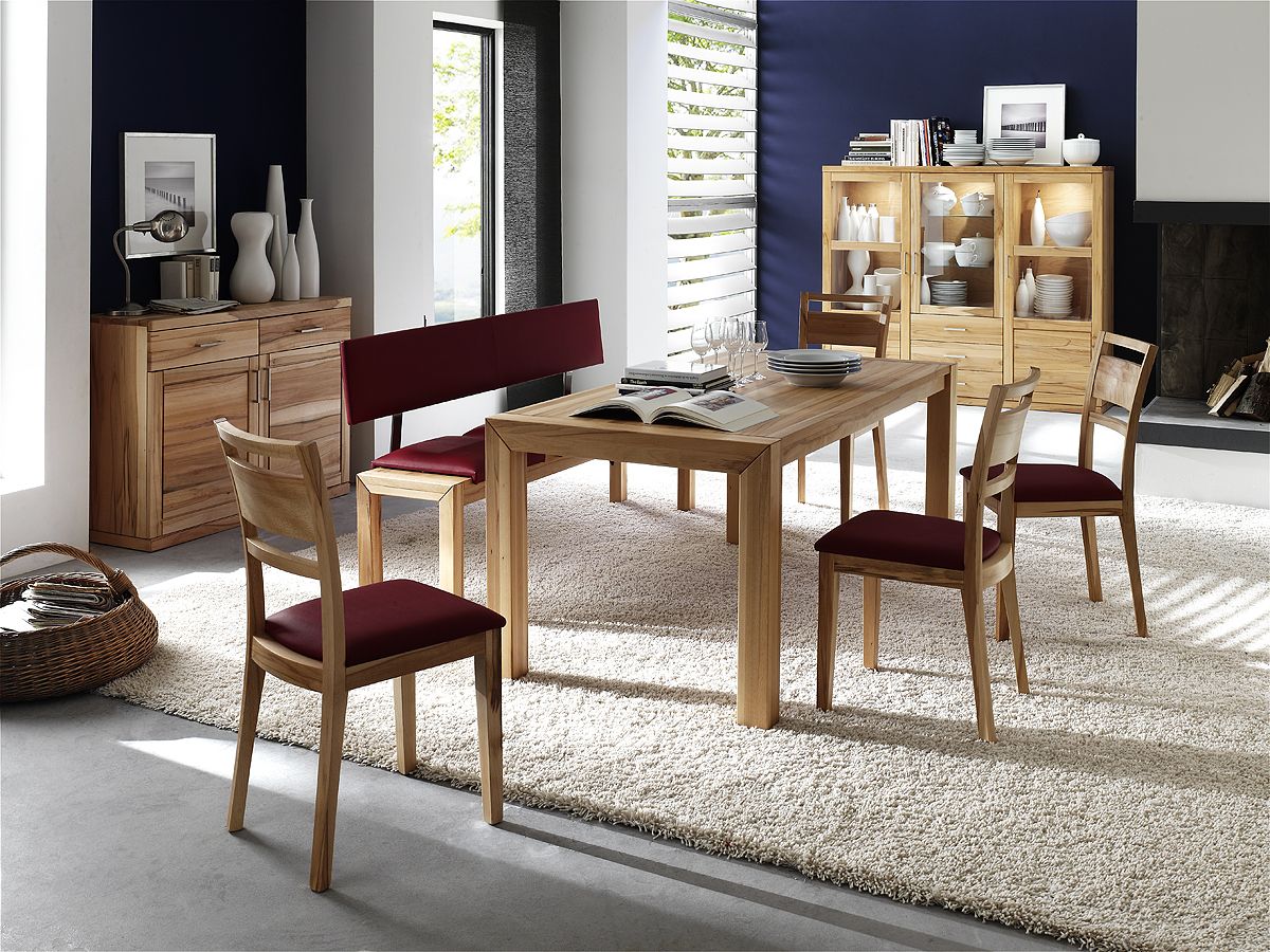 Esszimmer mit Holztisch und roten Stühlen und Bank, auf hellem Langflorteppich vor blau-weißer Wand.
