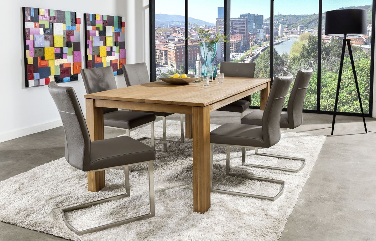 Holztisch mit sechs grauen Schwingstühlen auf weißem Teppich vor einer Fensterfront mit Stadtblick.