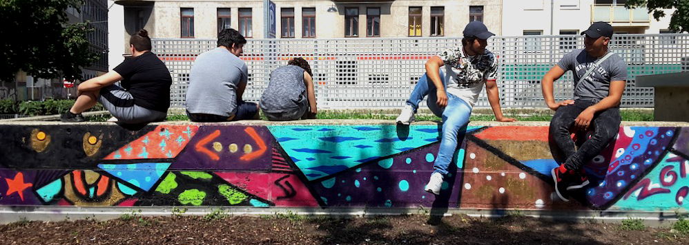 Fünf Jugendliche sitzen auf einer Betonmauer in einem Park