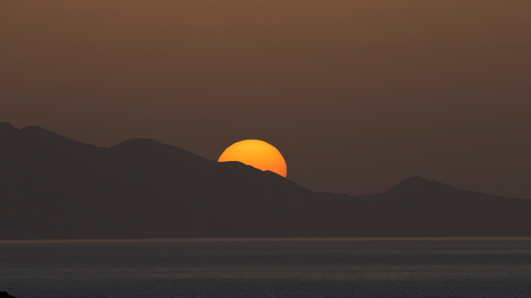 ... versinkt die Sonne langsam hinter einem Hügelzug am Meer.